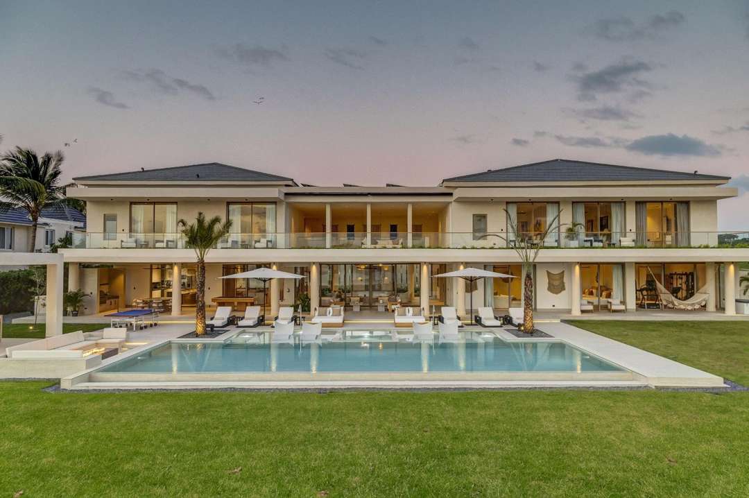 Modern luxury villa exterior at dusk with a large infinity pool, elegant sun loungers, and expansive terraces in Punta Cana.