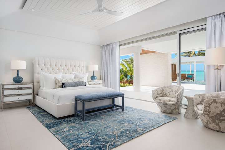 Luxurious master suite at Sole E Mare featuring a tufted king bed, blue rug, and private terrace with stunning ocean views.