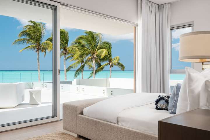 Contemporary master suite at Sole E Mare offering a plush bed and sliding glass doors opening to panoramic ocean views.