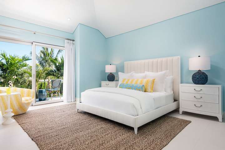 Bright guest bedroom at Sole E Mare with light blue walls, a plush white bed, and sliding doors to a lush garden terrace.