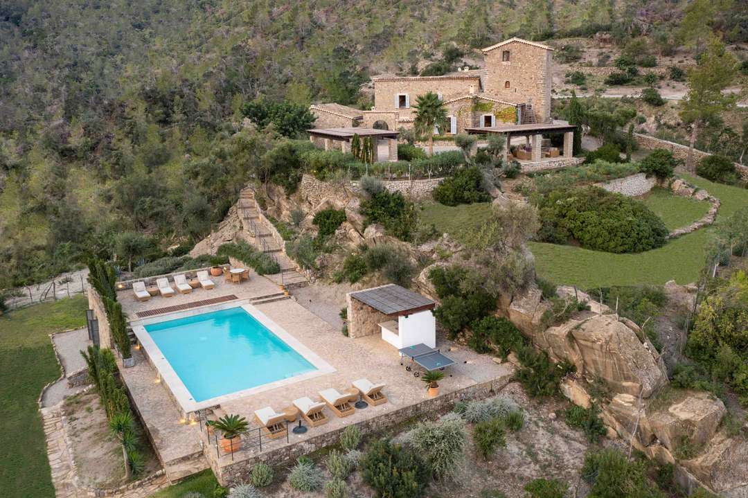 Aerial view of Son Balagueret, a historic stone villa with a private pool nestled in a lush Mallorcan hillside.