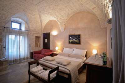Serene bedroom at luxury villa Sublimia featuring traditional vaulted stone ceilings, a red sofa, and refined decor.