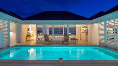 Serene central courtyard pool illuminated at night, framed by white louvered doors opening to a luxurious lounge.