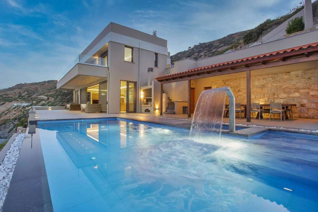 Luxury villa Suzette in Heraklion featuring a seawater infinity pool with waterfall, modern design, and alfresco dining.
