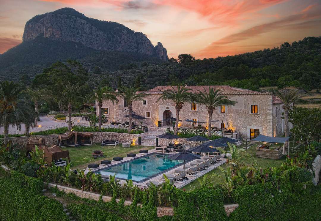 Aerial view of The Farm Mansion, a historic stone villa with a private pool, palm trees, and breathtaking mountain sunsets.