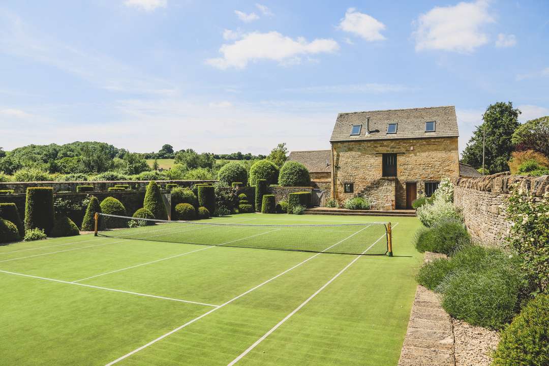 Private tennis court at The Granary, surrounded by Jinny Blom landscaped gardens and historic Cotswold stone architecture.