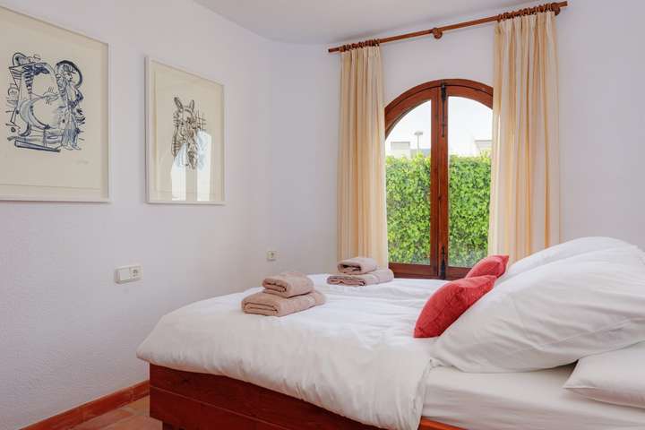 Elegant double bedroom featuring crisp white linens, terracotta floors, and a charming arched window framing garden views.