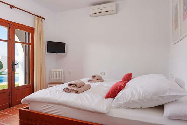 Master bedroom with a double bed, terracotta floors, air conditioning, and arched wooden doors opening to the pool area.