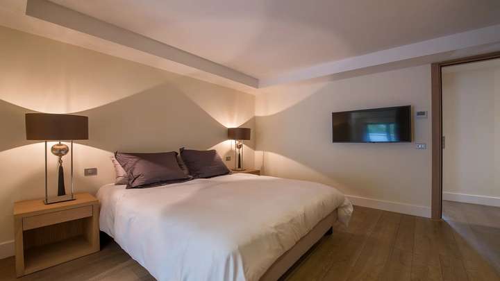 Elegant double bedroom at The Town House in St Tropez, featuring hardwood floors, modern lighting, and a flat-screen TV.