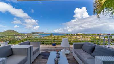Elegant outdoor lounge at luxury Villa Ti Agave featuring woven sofas on a rich wooden deck with panoramic ocean views.