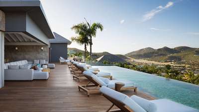 Expansive wooden terrace featuring a 20-meter infinity pool, elegant sunbeds, and outdoor lounge with panoramic ocean views.