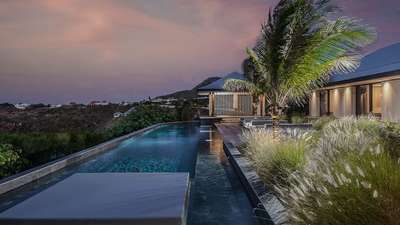 Magnificent 80-foot heated granite pool and elegant wooden deck with a yoga ajoupa at dusk in Pointe Milou, St-Barthelemy.