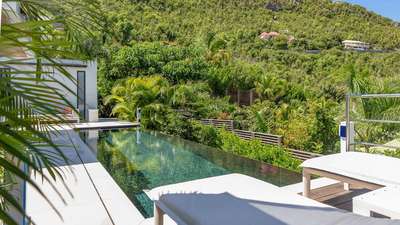 Infinity heated pool at Ventura Estate in St-Barths, featuring sleek white sun loungers and lush tropical hillside views.