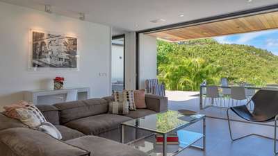 Expansive living area with plush seating seamlessly transitioning to a sunlit terrace and vibrant tropical landscape.