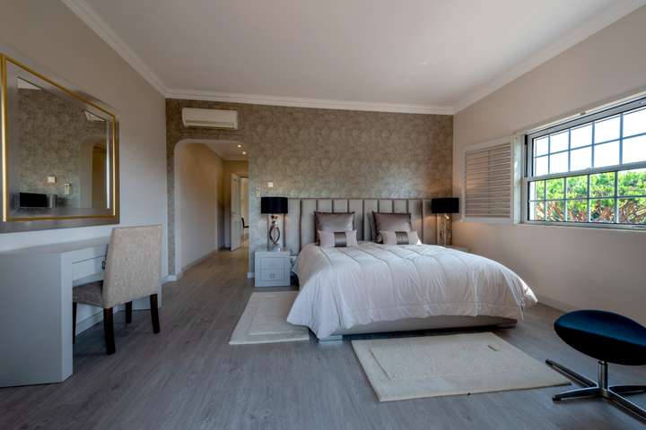 Elegant bedroom at Villa Atlantico featuring textured wallpaper, a plush double bed, and a window framing lush garden views.