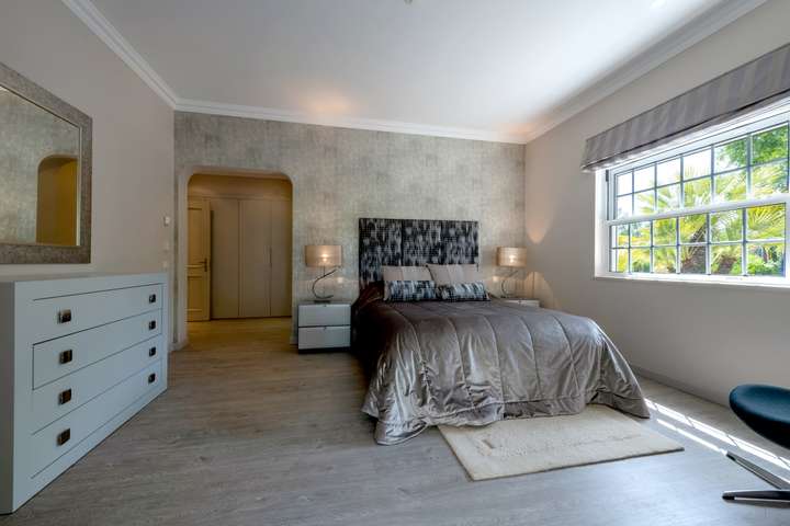 Luxurious bedroom showcasing a velvet bedspread, silver textured wallpaper, and a bright window with tranquil garden views.