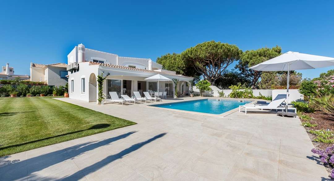 Luxury white villa in Quinta do Lago featuring a private pool, sun terrace, and manicured garden under a clear blue sky.