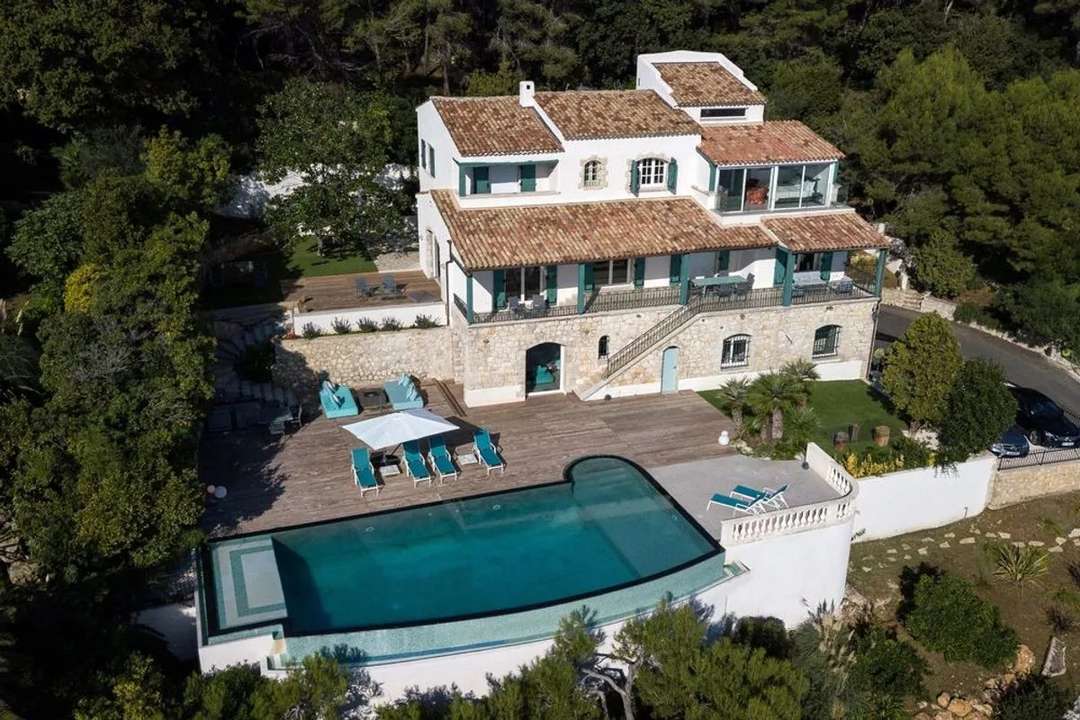 Aerial view of luxury Villa Acacia in Cannes, featuring a stunning infinity pool, wooden deck, and elegant stone facade.