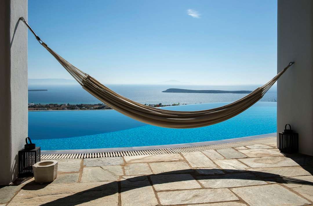 Relax in a hammock by the luxurious infinity pool at Villa Adonis, enjoying panoramic Aegean Sea views and serene island vibes.