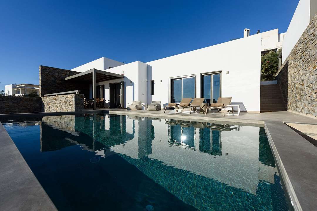 Private pool reflecting Limani Wander's white Cycladic architecture and natural stone walls on a sunlit terrace in Paros.
