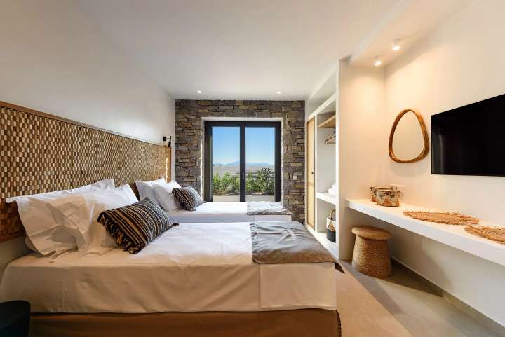 Stylish twin bedroom featuring natural stone walls, a woven headboard, and sliding glass doors leading to the outdoor terrace.