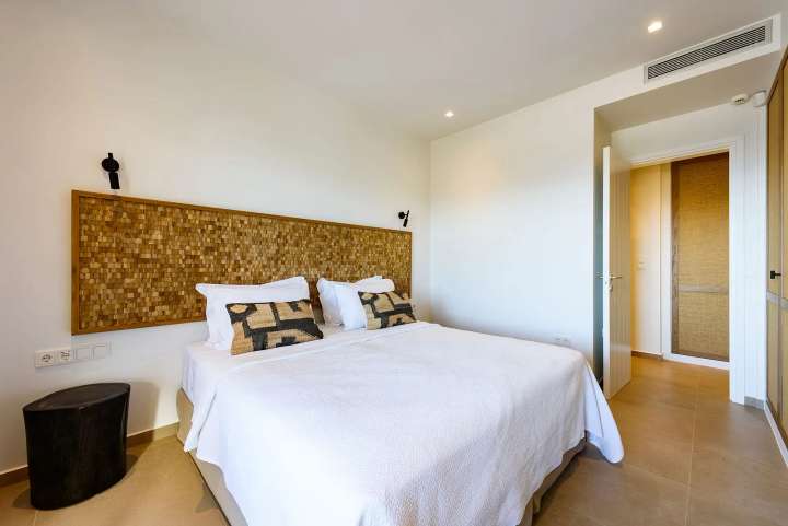 Elegant double bedroom featuring a handcrafted woven headboard, crisp white linens, and modern Cycladic design elements.