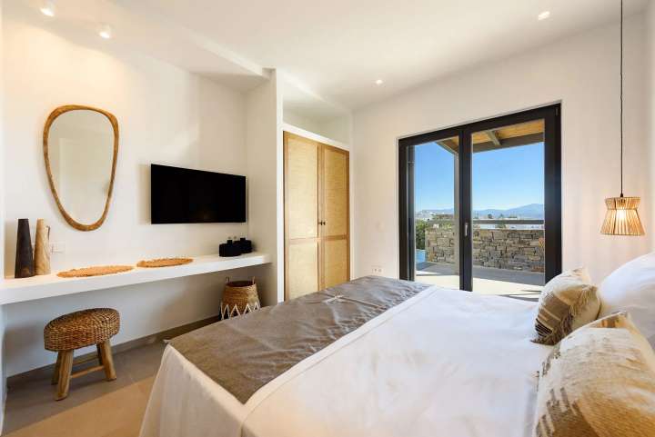 Serene double bedroom with curated lighting, woven decor, and sliding glass doors opening to a private sea view terrace.