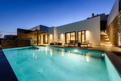 Illuminated private swimming pool and outdoor terrace at night, featuring contemporary Cycladic design and alfresco dining.