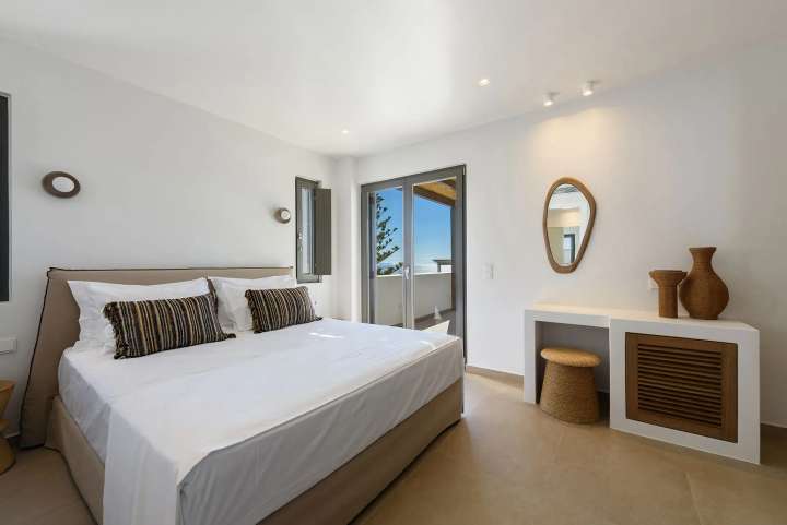 Bright double bedroom with natural textures, sliding doors, and a private balcony offering stunning Aegean Sea views.