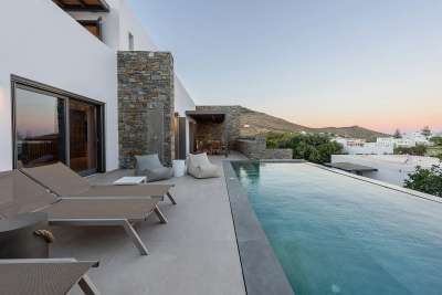 Serene private pool terrace at dusk featuring elegant loungers, natural stone walls, and beautiful Paros mountain views.