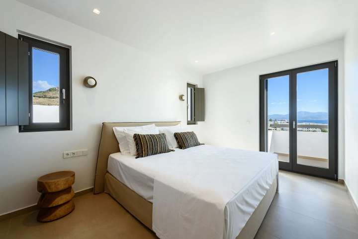 Bright double bedroom with clean white interiors and large glass doors opening to a private balcony with stunning sea views.