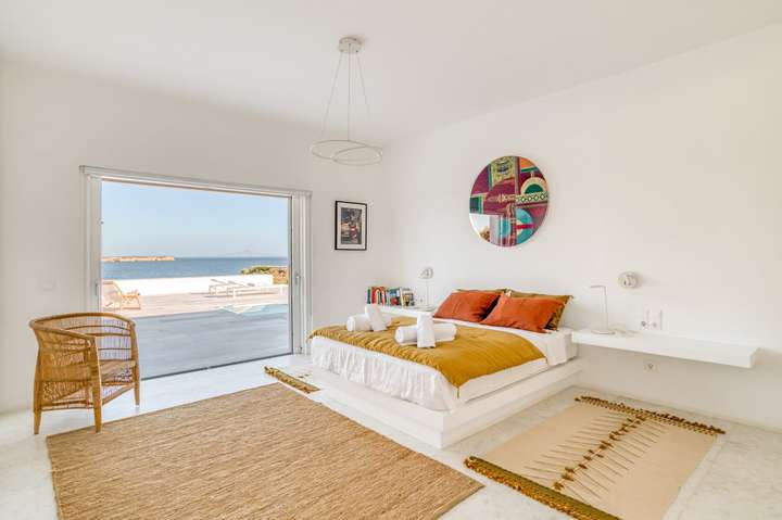 Elegant double bedroom at Villa Hermes featuring contemporary decor and sliding doors opening to a stunning sea view terrace.