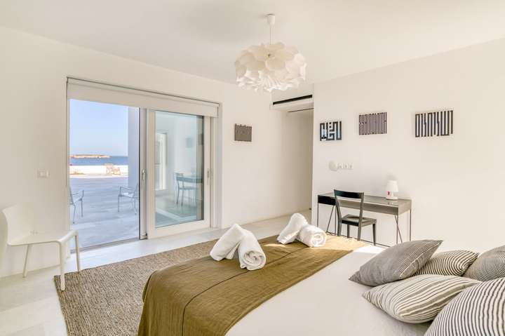 Contemporary double bedroom at Villa Hermes offering minimalist decor, a sleek desk, and direct access to a sea view terrace.