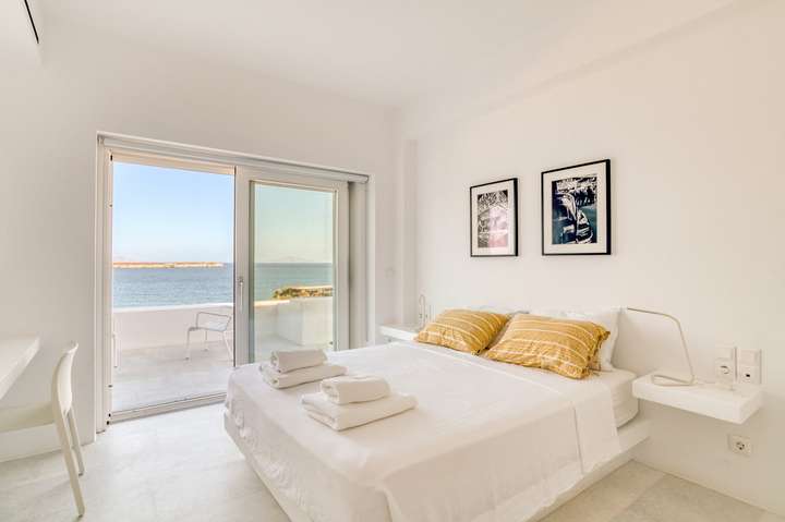 Luxurious double bedroom at Villa Hermes with minimalist white decor and sliding doors opening to panoramic Aegean Sea views.