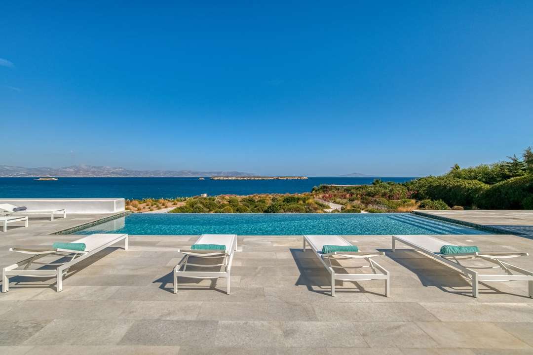 Stunning infinity pool at Villa Hermes with elegant white loungers and breathtaking panoramic views of the Aegean Sea.