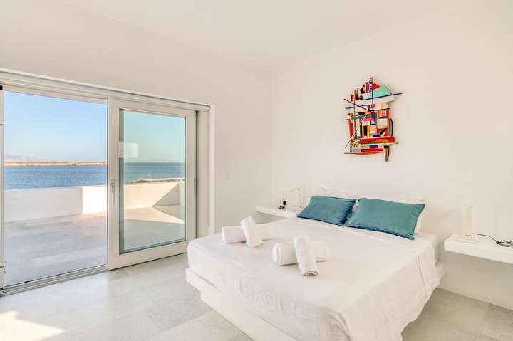 Chic double bedroom at Villa Hermes with vibrant art, crisp white linens, and a private balcony offering stunning sea views.
