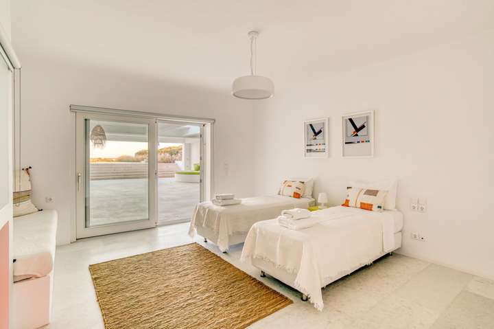 Elegant twin bedroom at Villa Hermes with minimalist white decor and sliding glass doors opening to the sunlit terrace.