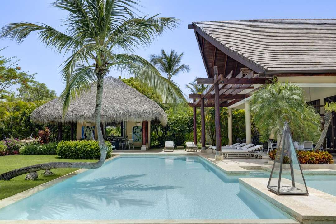 Elegant private pool at Villa Caballet in Punta Cana, featuring a thatched palapa, lush gardens, and chic sun loungers.
