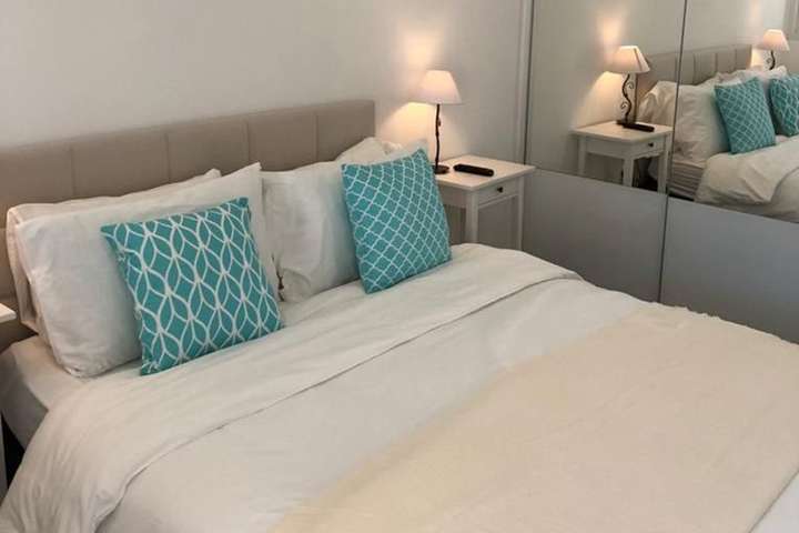 Elegant bedroom at Villa Cap with a tufted headboard, mirrored closets, and crisp white bedding accented by teal pillows.