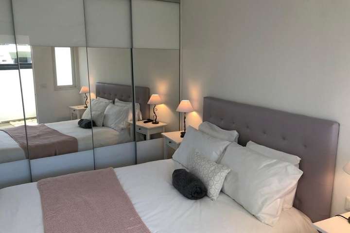 Luxurious bedroom at Villa Cap featuring a plush grey headboard, mirrored wardrobes, and elegant linens with a pink throw.