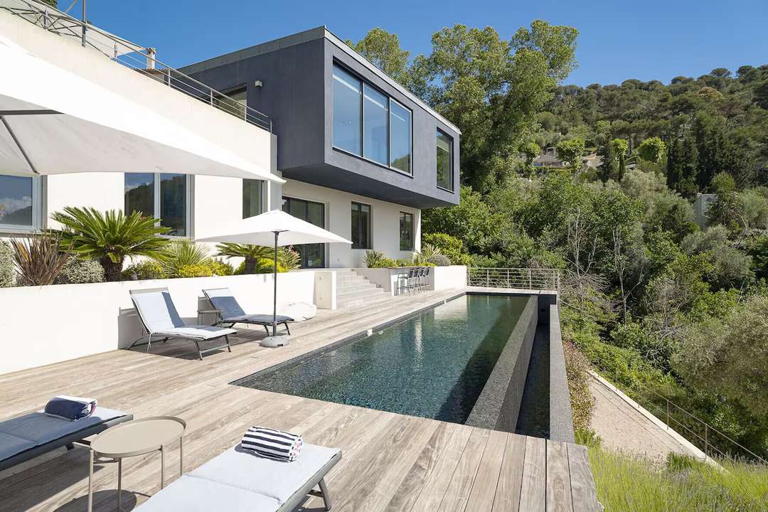 Contemporary luxury villa in Eze featuring a sleek infinity pool, wooden sun deck, and lush Mediterranean nature views.