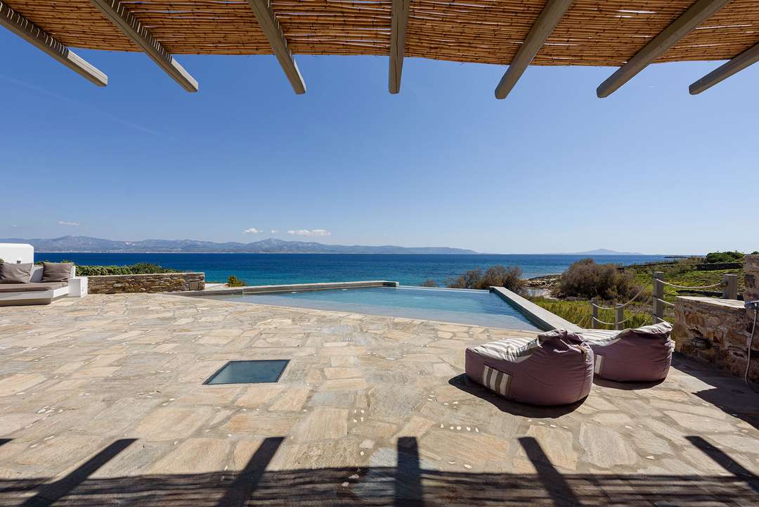 Stone terrace with bamboo pergola, infinity pool, and bean bags offering panoramic Aegean Sea views at Villa Athena.