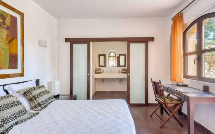 Elegant double bedroom offering a comfortable bed, wooden desk, and sliding frosted doors to a spacious ensuite bathroom.