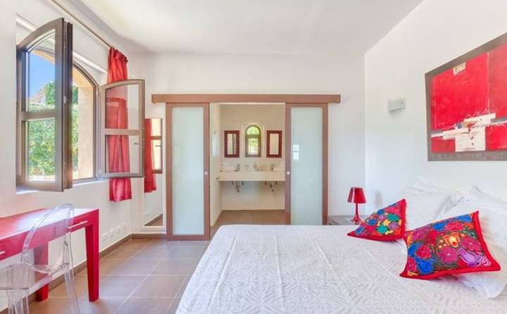 Elegant double bedroom featuring a plush bed, vibrant red accents, and sliding glass doors to a modern ensuite bathroom.
