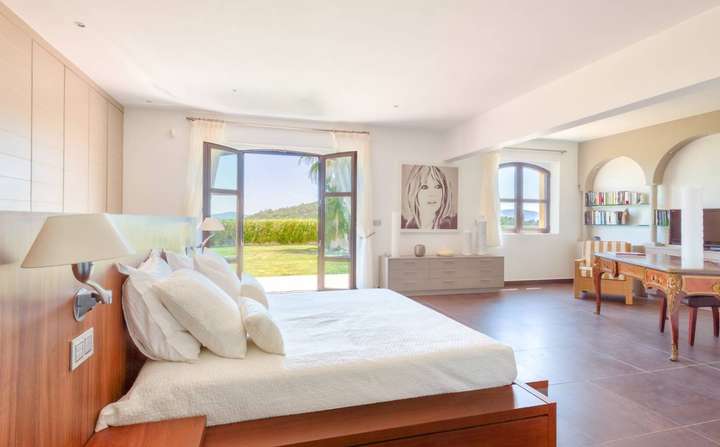 Spacious master bedroom at Villa du Paradis featuring a plush bed, office area, and French doors opening to the lush garden.