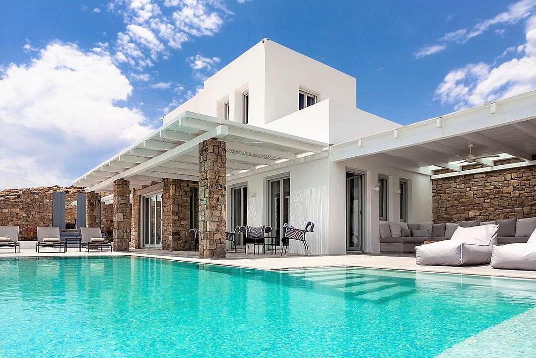 Magnificent infinity pool at Villa Elis in Mykonos, featuring white Cycladic architecture, stone pillars, and elegant lounging.