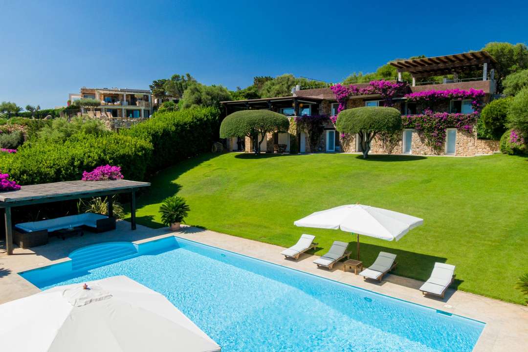 Elegant stone villa Girella featuring a large private pool, manicured garden, and covered lounge area in Porto Rotondo.