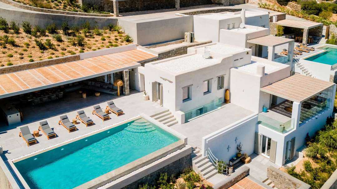 Aerial view of Villa Harmonia's modern Cycladic architecture, sleek infinity pool, and shaded outdoor lounge in Drios.