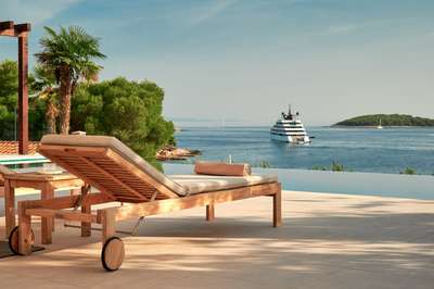 Premium wooden sun lounger by the heated pool, offering uninterrupted views of the Adriatic Sea and passing luxury yachts.