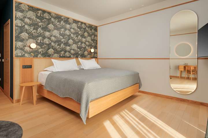 Bright luxury bedroom featuring a king-size bed with a wooden frame, elegant patterned headboard, and a large modern mirror.